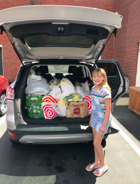 Little girl loads donation groceries into car