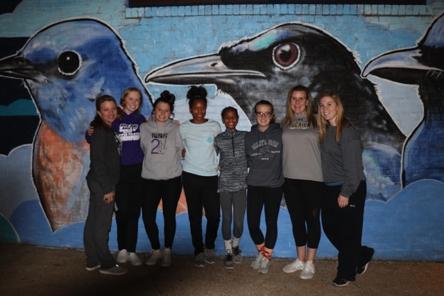 Group of Shelter KC volunteers poses in front of mural of birds
