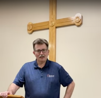 Shelter Kc Employee talking in front of podium with large cross behind him