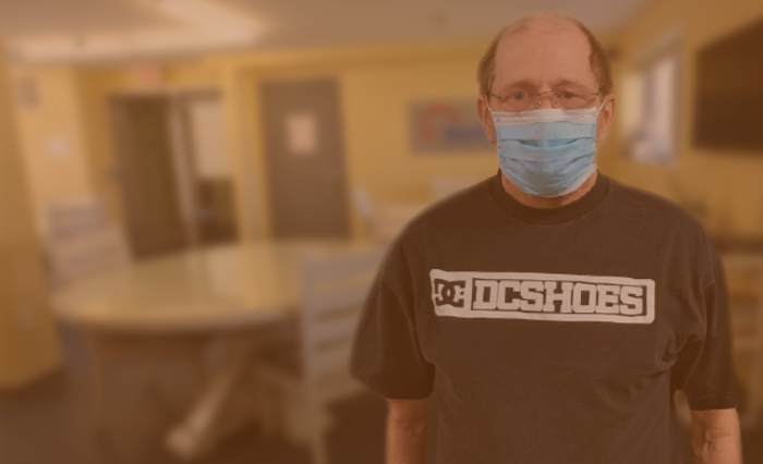 Man in mask with glasses in front of break room blurred background
